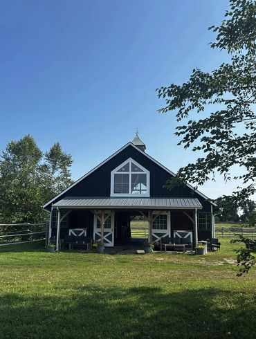 Black barn with white trim under a clear blue sky on a sunny day.