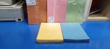 Stacks of colorful paper folders on a blue floor near a printer and shelf.