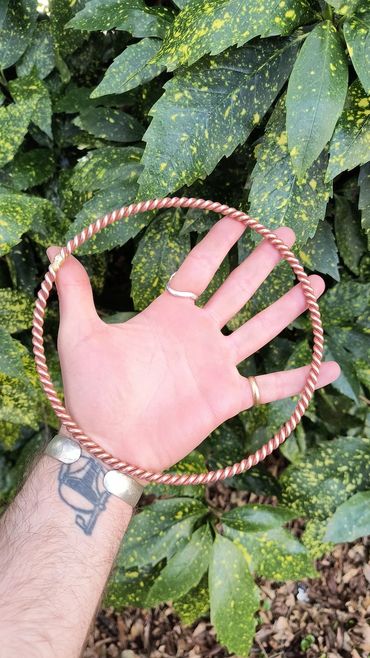 Hand holding a twisted copper bracelet against green foliage background.