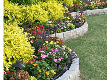 A curved garden bed with colorful flowers and green shrubs bordered by stone.