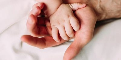 Adult hand holding a baby's hand gently.