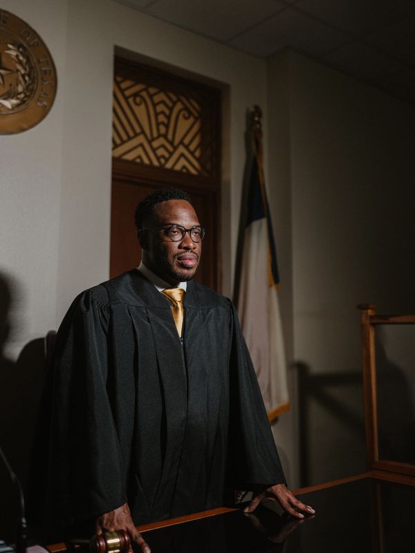 Judge in black robe stands confidently in courtroom with gavel.