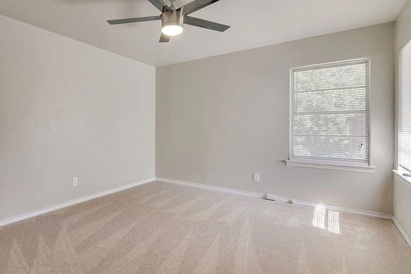 The guest bedroom is unfurnished, with three windows, a ceiling fan, and new carpet.