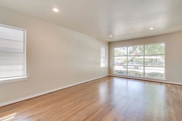 Large living room with new hardwood floors and three large windows allowing natural sunlight inside.