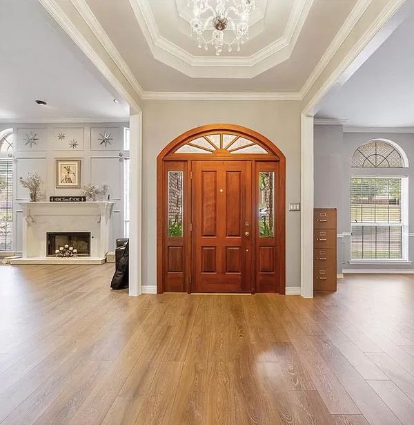 The residential grand entrance features windows, a fireplace, and lightly colored hardwood floors.