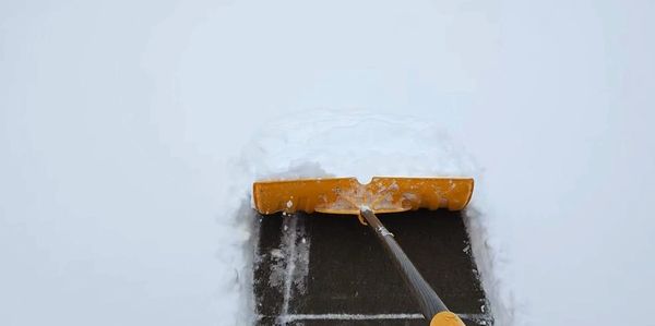 A snow shovel clearing a path on a driveway covered with snow.