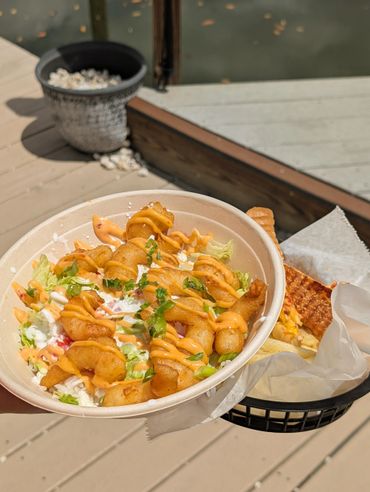 A fresh shrimp bowl with sauce and a sandwich in the background.