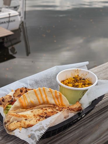 Grilled fish taco with a side of seasoned corn by the water.