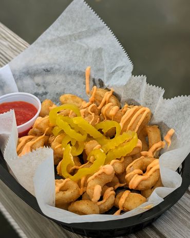 Basket of fried calamari with spicy mayo and pepper rings, served with cocktail sauce.