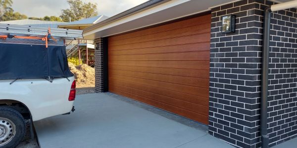 Modern wooden garage door beside white vehicle and brick wall.