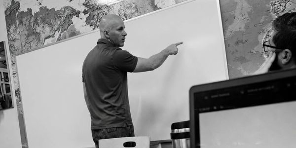 Man pointing at a whiteboard during a discussion in a casual office setting.