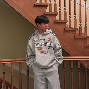 Young man in grey hoodie and sweatpants standing by wooden staircase.