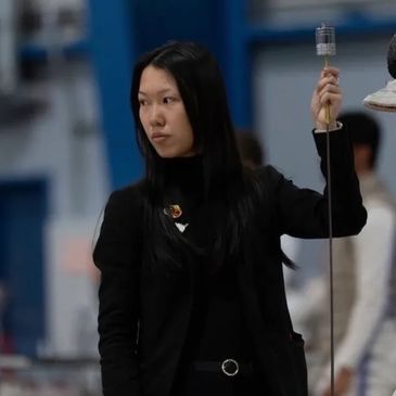 Woman in black holding a fencing sword indoors.