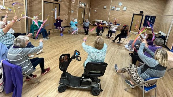 Group of older adults participating in seated dance exercise with ribbons.