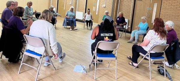 Group fitness class with seated participants and instructor.