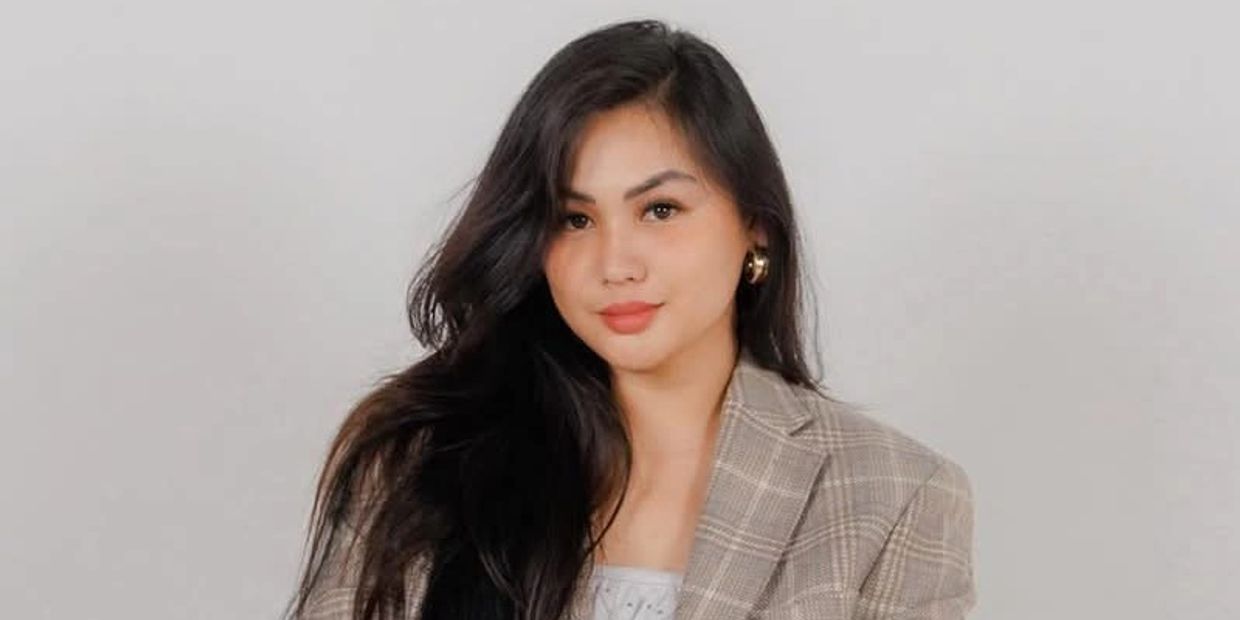Smiling woman with long black hair in a plaid blazer.