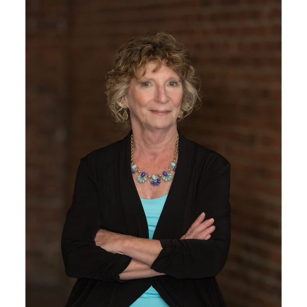 Confident older woman with curly hair wearing a black cardigan and turquoise necklace.