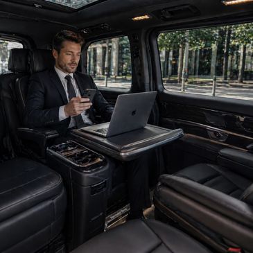 Businessman using laptop and smartphone inside a luxury car.