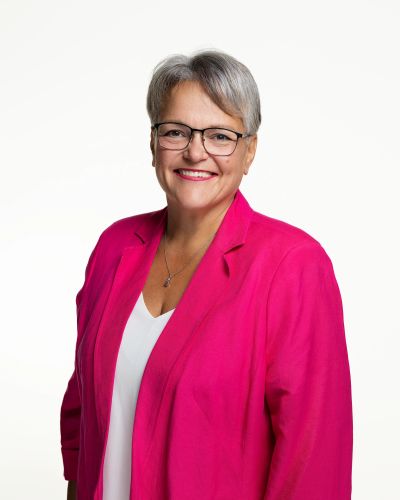 Smiling woman in a bright pink blazer and glasses.