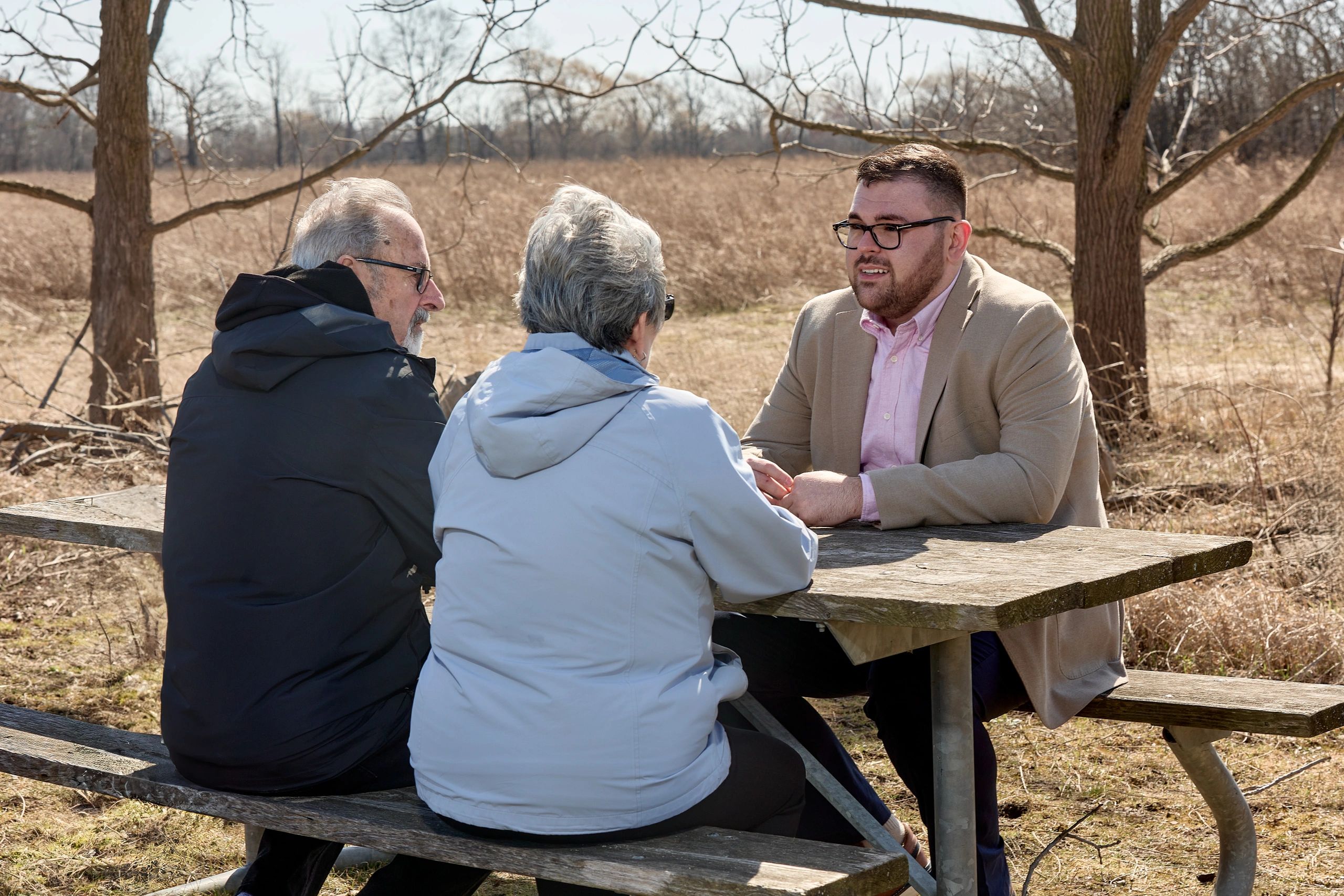 Three people having a serious conversation at a picnic table outdoors.