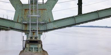 Close-up of a green metal bridge structure over a wide river under a cloudy sky.