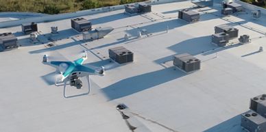 A drone flying over a rooftop with HVAC units casting shadows.