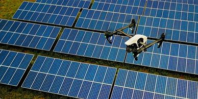 Drone flying over solar panels in a green field.