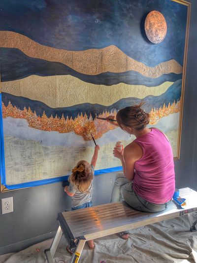 Connie works on an indoor paper mountain mural while her toddler daughter paints along with her.