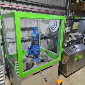 Industrial testing machine with a green-framed enclosure.