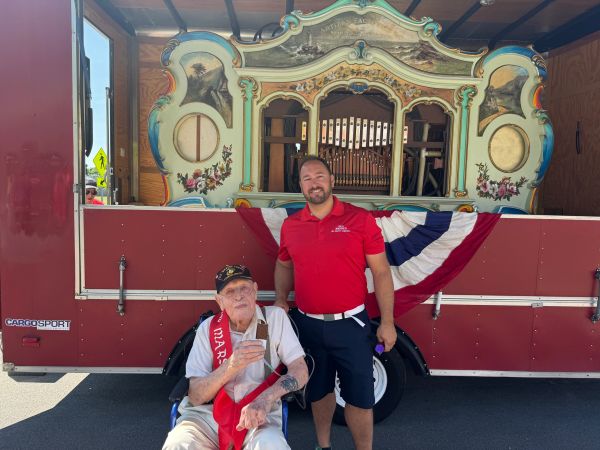 Veteran in a wheelchair with a man standing next to him in front of a decorated trailer.