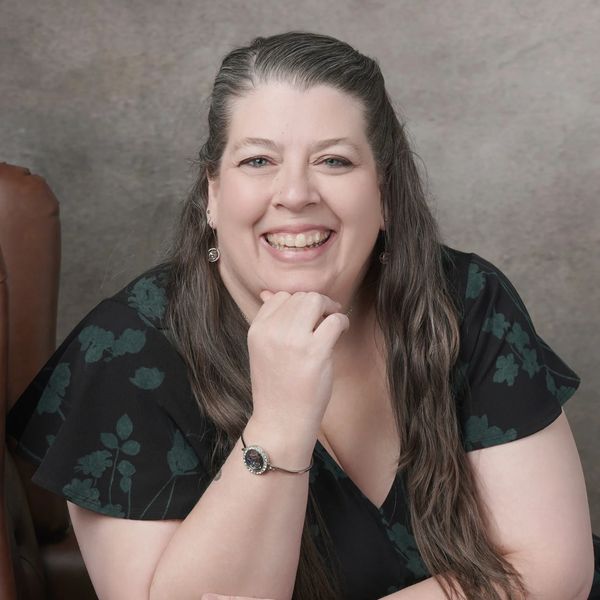 Smiling woman with long hair resting her chin on her hand.