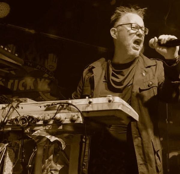 Man passionately singing and playing keyboard on stage.