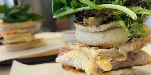 Stacked sandwich with melted cheese, ham, greens, and a fried egg on toasted bread.