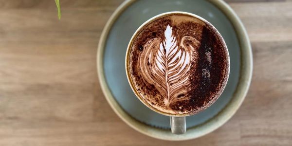 Top view of a cup of coffee with leaf-shaped latte art on a wooden table.