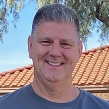 Smiling man outdoors with tiled roof background.