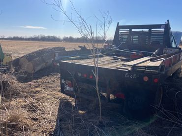 Flatbed truck loaded with tools parked in a sunny rural field.