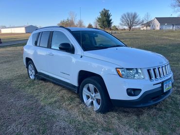 White Jeep Compass parked on grass under clear blue sky.