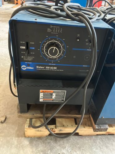 Miller Dialarc 250 AC/DC welding power source with cables on a wooden pallet.
