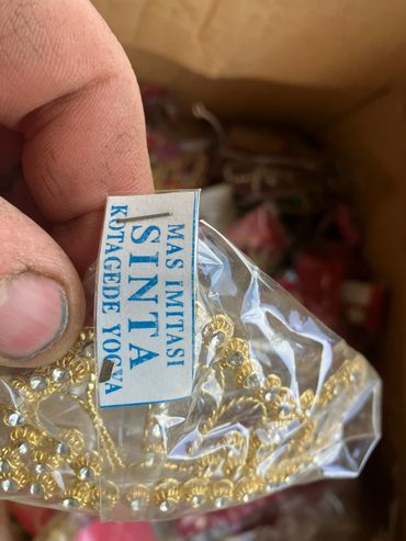 Hand holding a plastic bag with imitation gold jewelry and a label.