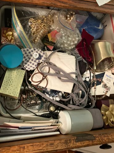 Drawer filled with jewelry, ribbons, and miscellaneous items.