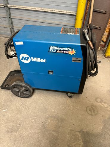 Blue Miller Millermatic 212 Auto-Set welding machine on wheels with cables.