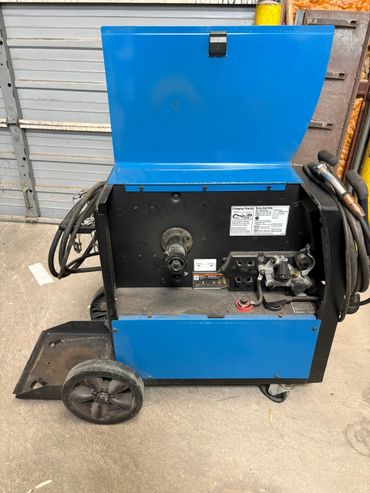 Blue welding machine with open panel and attached cables on wheels.