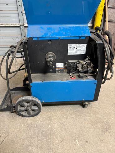 Blue welding machine with open panel showing internal components and cables.
