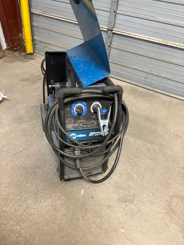 A Miller Millermatic 212 Auto-Set welding machine with cables coiled around the front.