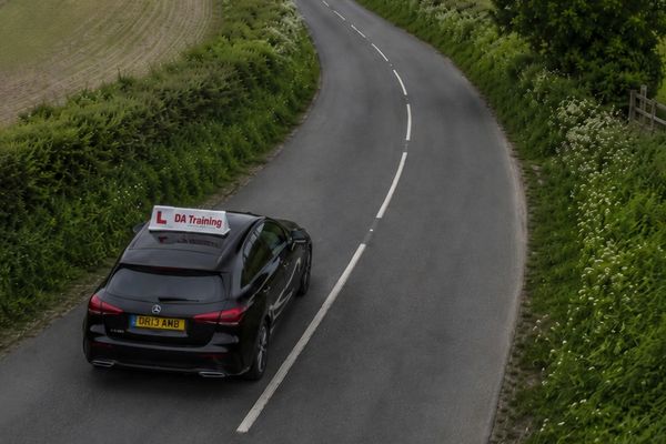 Black car with L-plates driving on a winding country road.