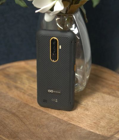 Black smartphone with gold edges standing on a wooden surface.