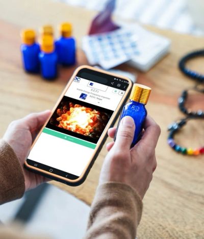 Person holding a blue bottle and smartphone displaying a product page with similar bottles in the background.