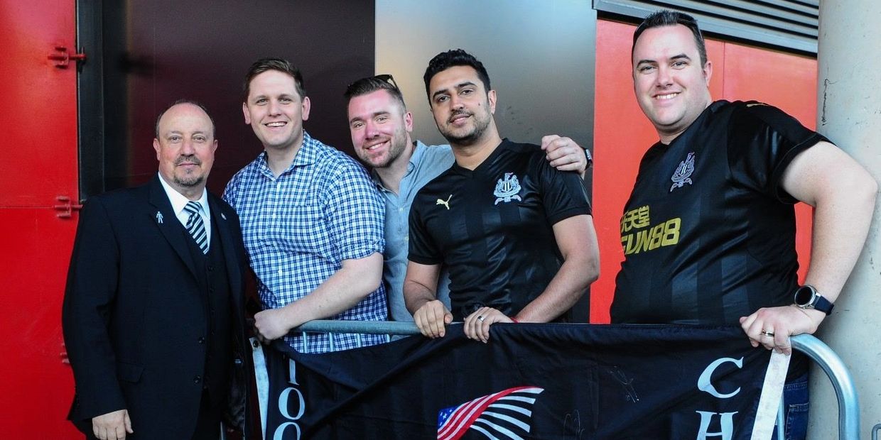 Five men posing with a flag, smiling at the camera.