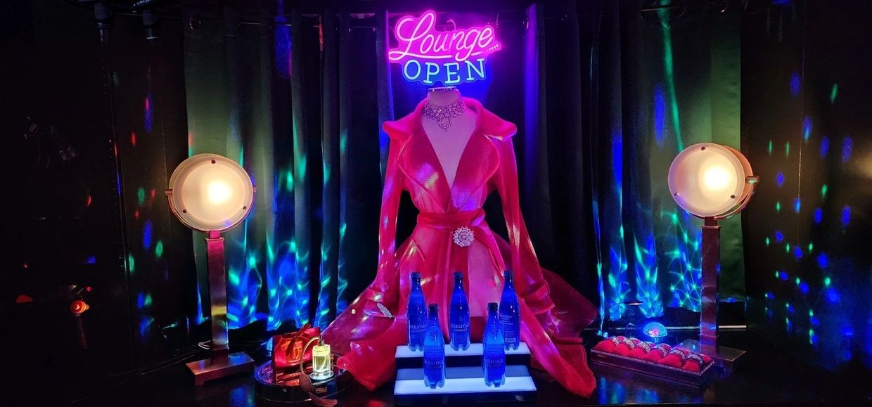 Neon-lit lounge display with mannequin and blue bottles.