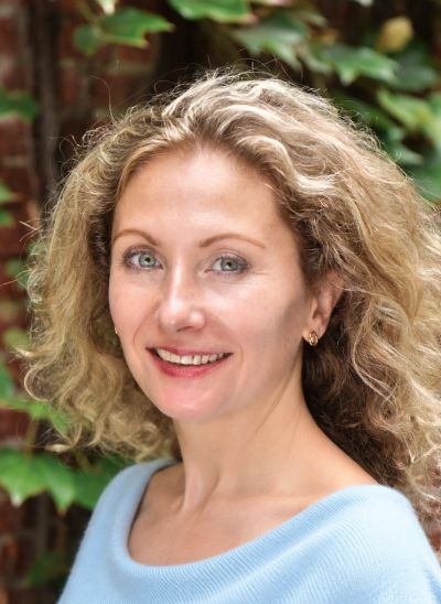 Smiling woman with curly blonde hair outdoors.